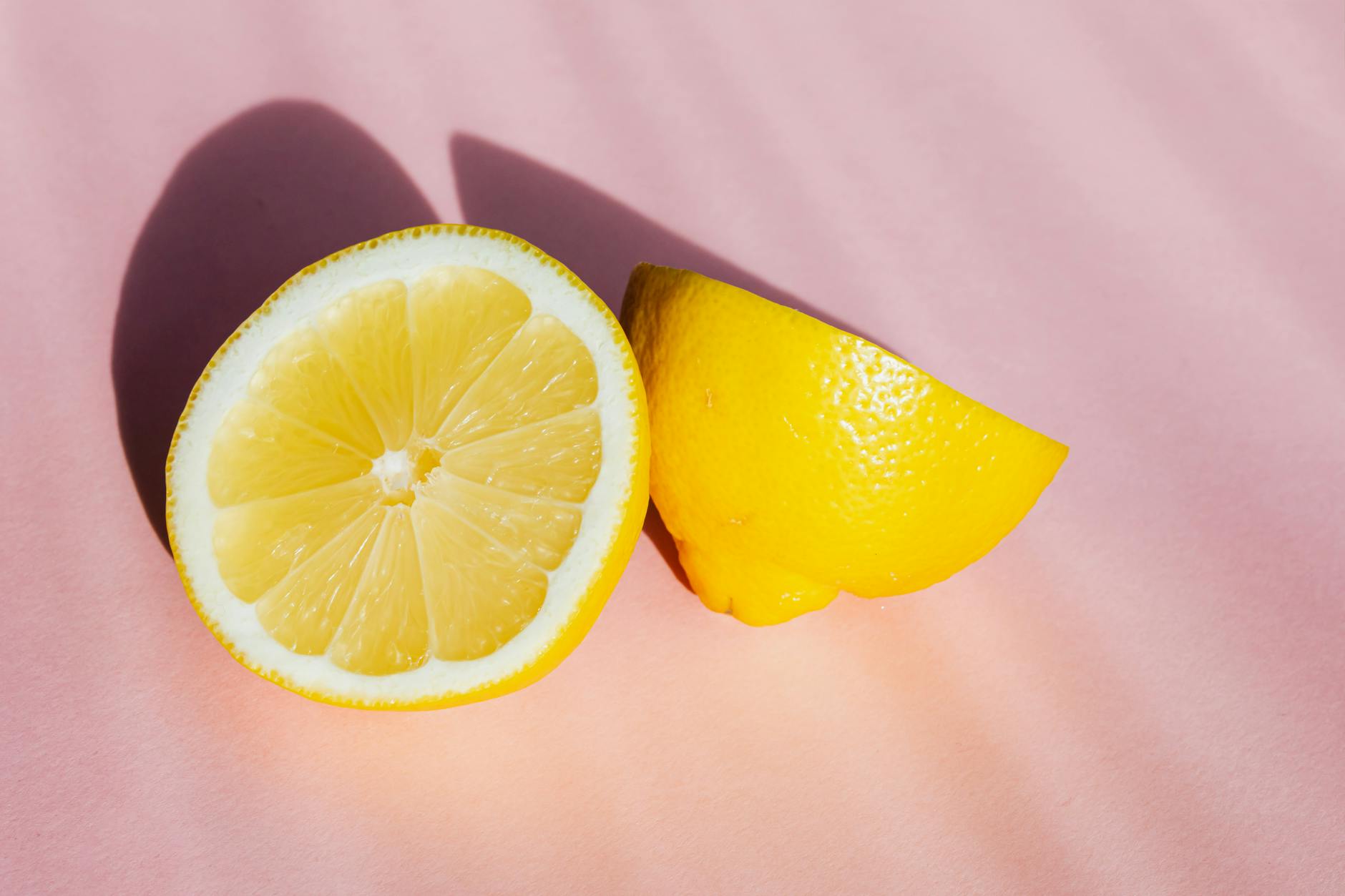 Fresh lemon halves on a soft pink background in bright light