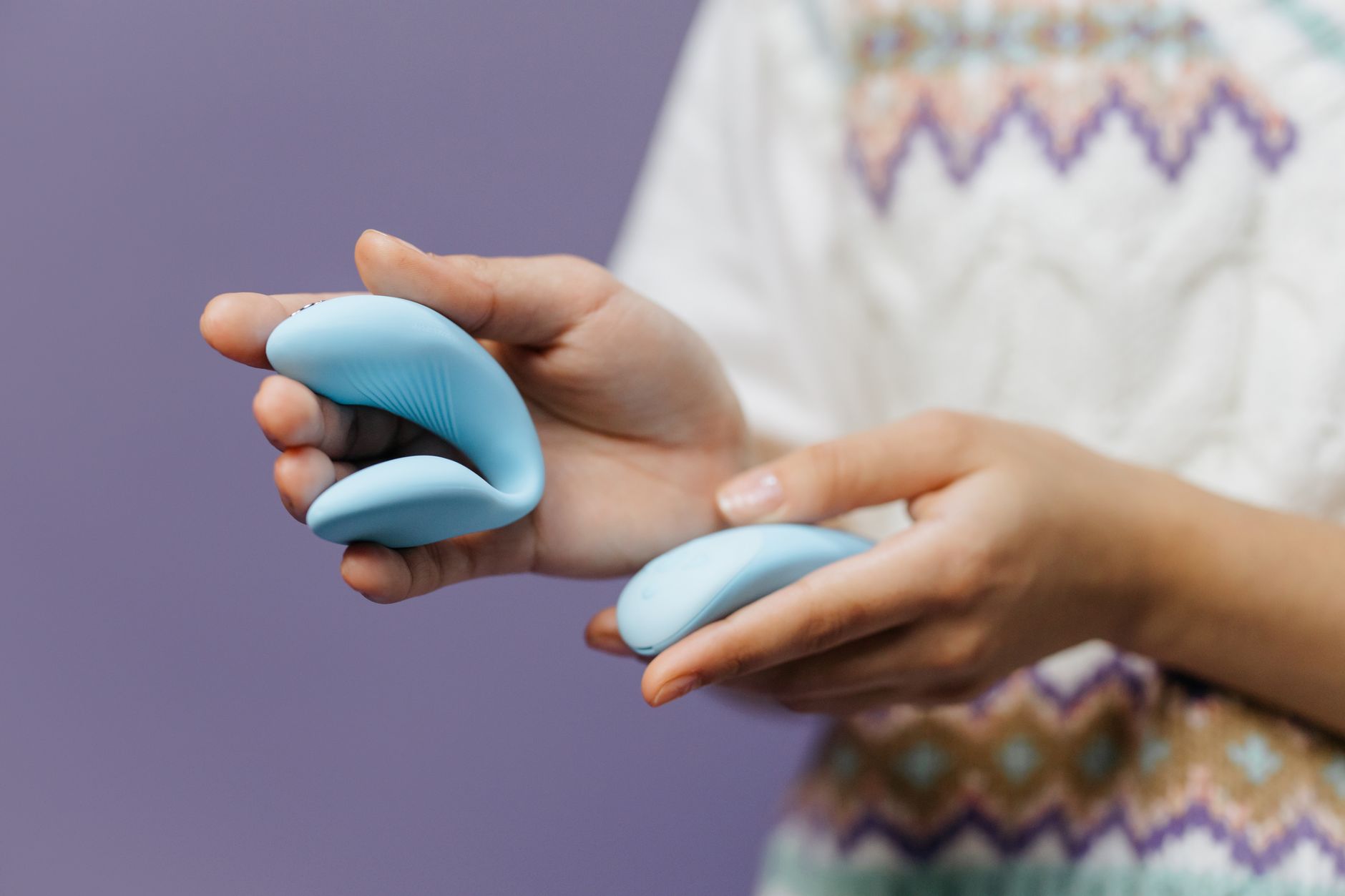 Mão segurando vibrador azul elegante contra fundo roxo