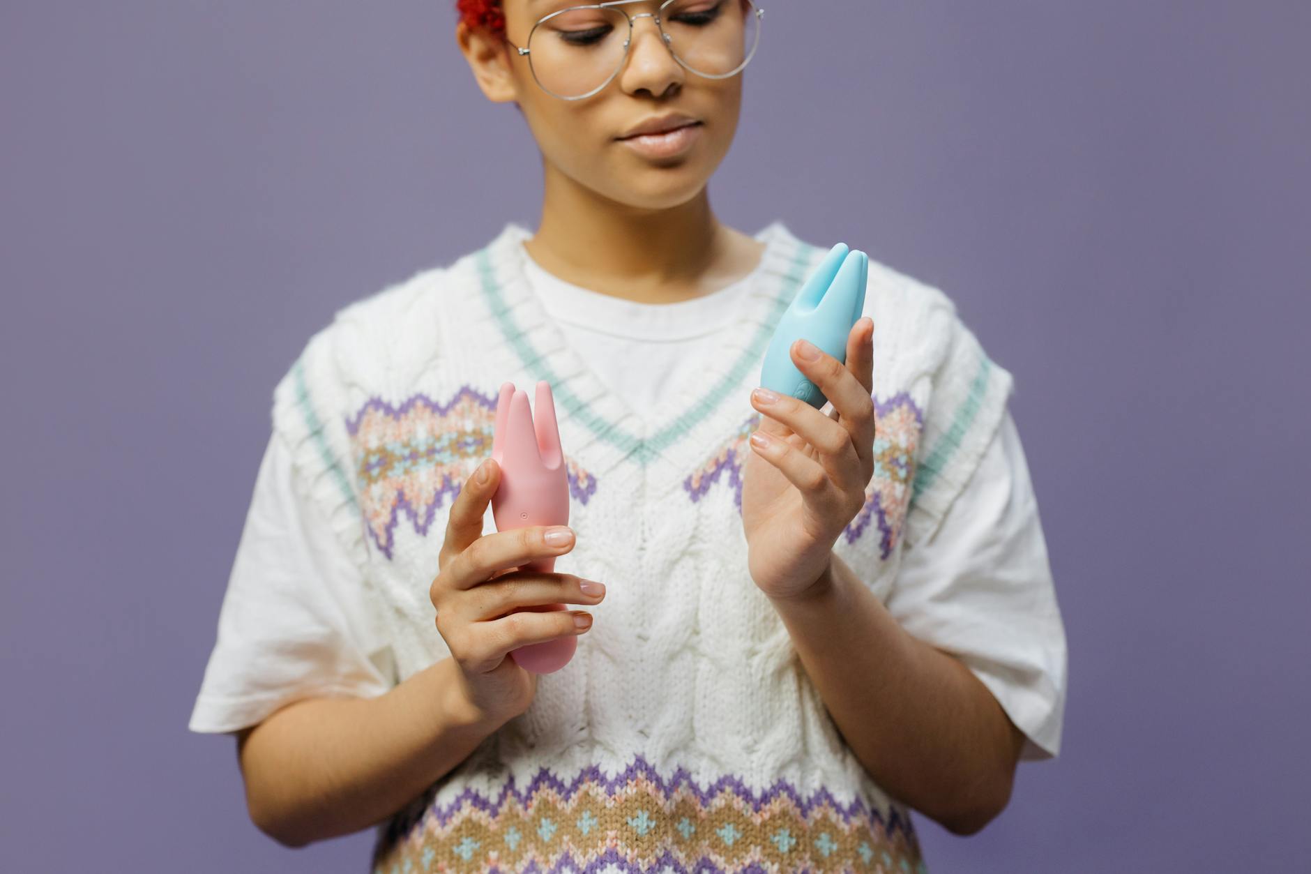 Mulher com óculos segurando vibradores de silicone azul e rosa de forma contemplativa