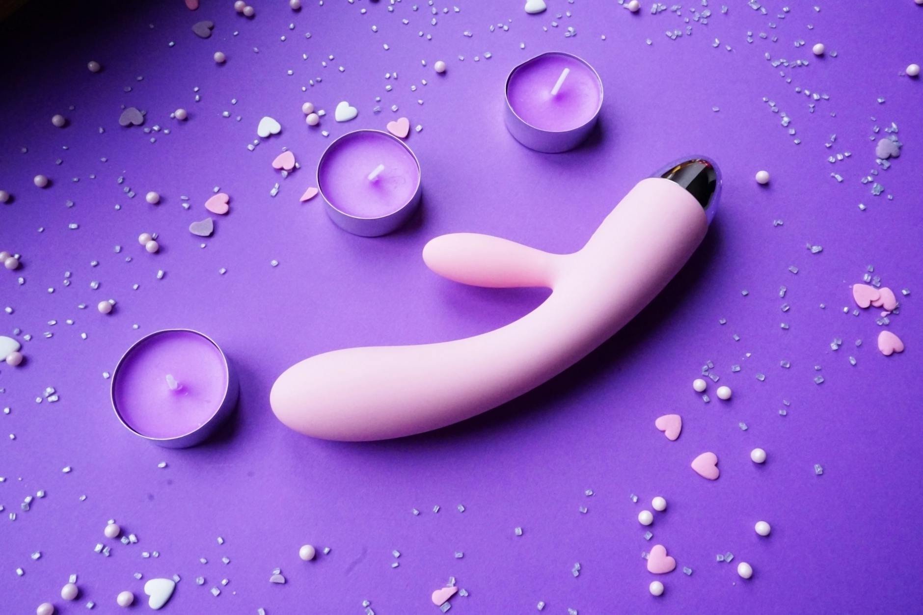 Vibrador de sucção de limão em fundo roxo com confete em forma de coração e velas para criar uma atmosfera romântica